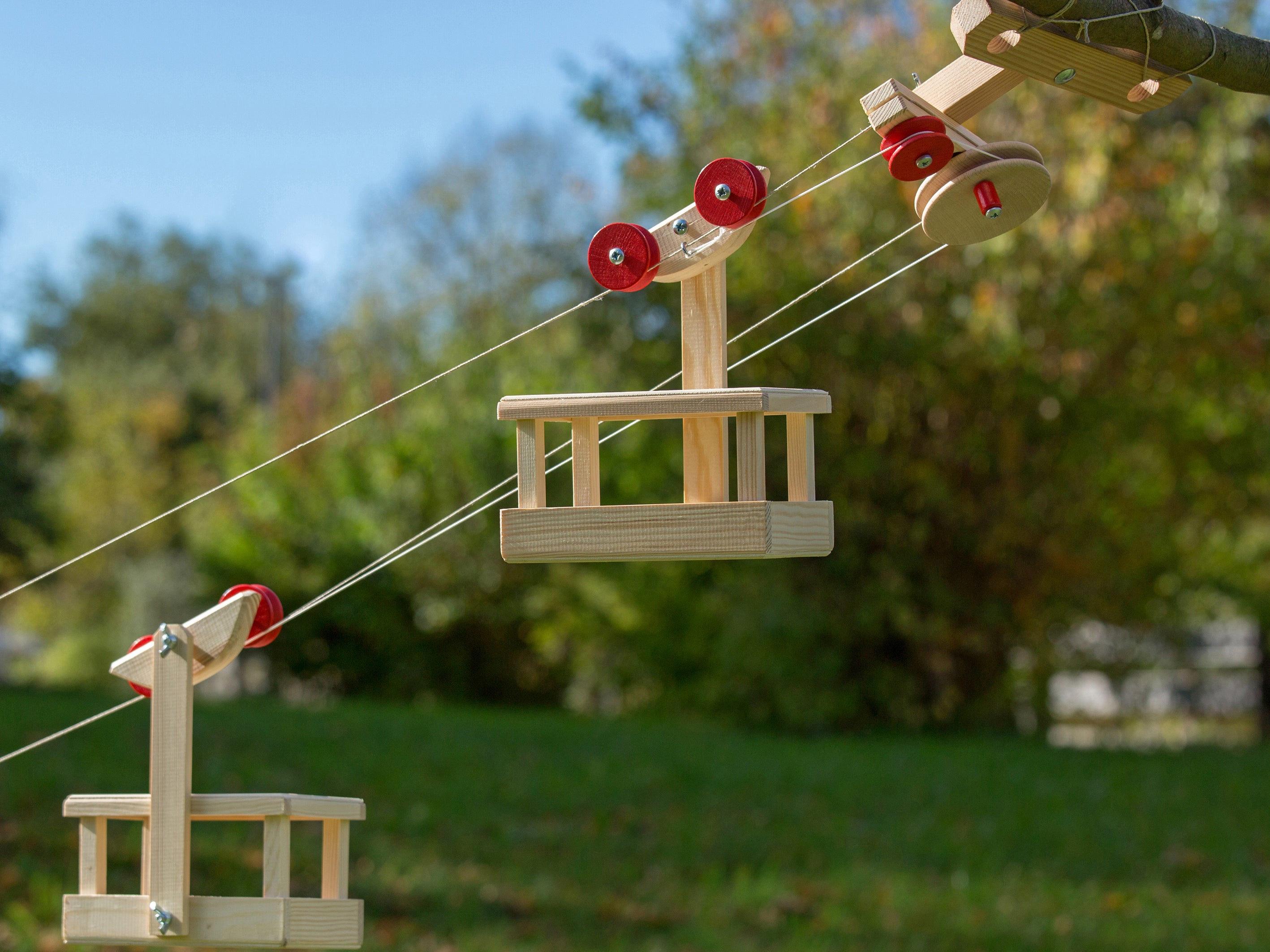 Wooden swing set with red seats hanging from ropes in a park setting.