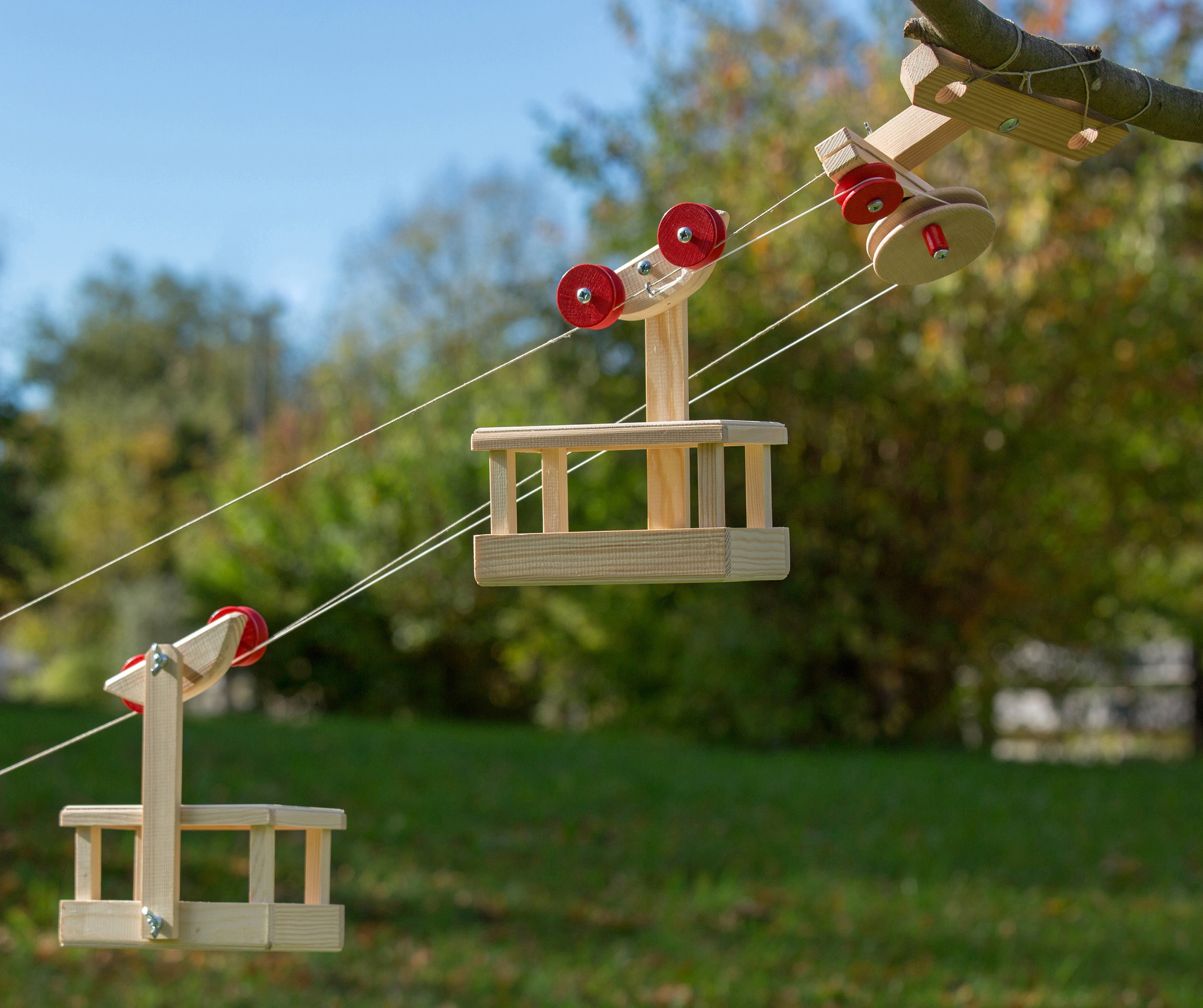 Wooden swing set with red seats hanging from ropes in a park setting.