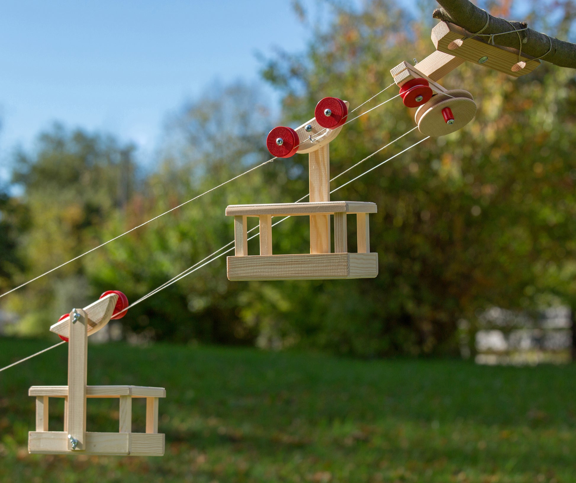Wooden swing set with red seats hanging from ropes in a park setting.