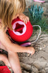 Child playing with a red bucket on a sandy surface