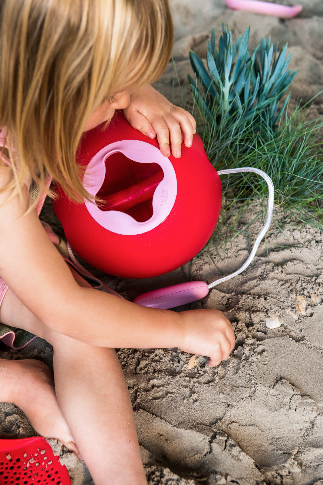 Child playing with a red bucket on a sandy surface
