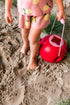 Child playing in sand with a red bucket 