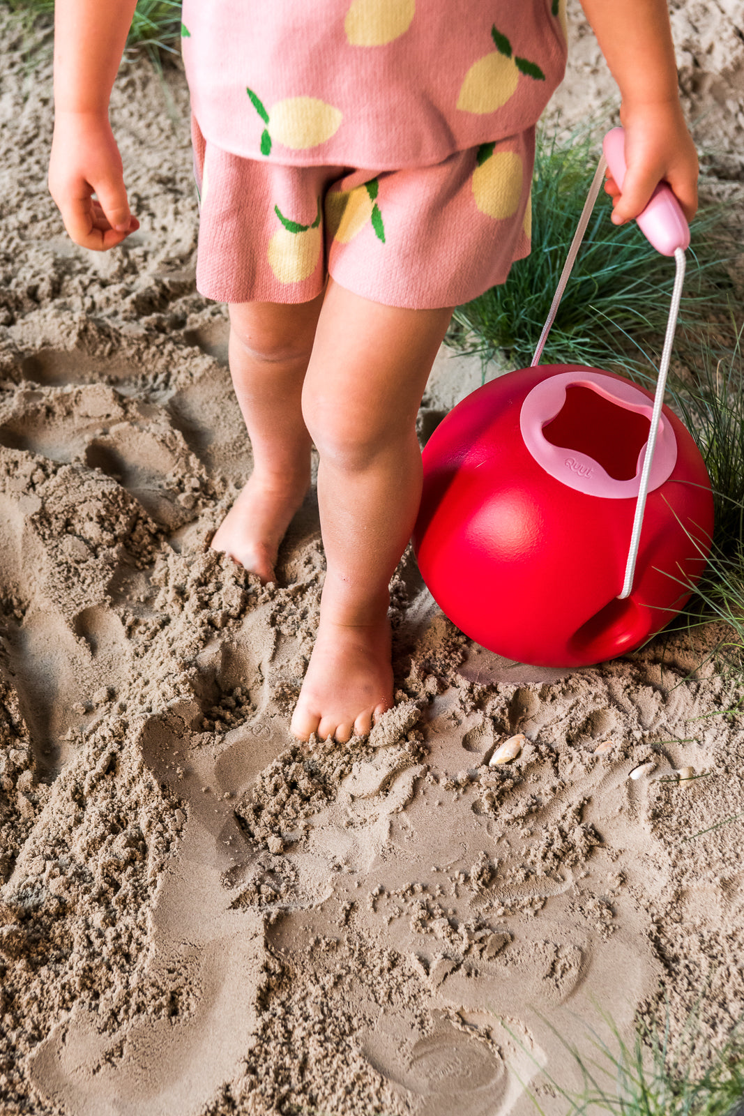 Child playing in sand with a red bucket 