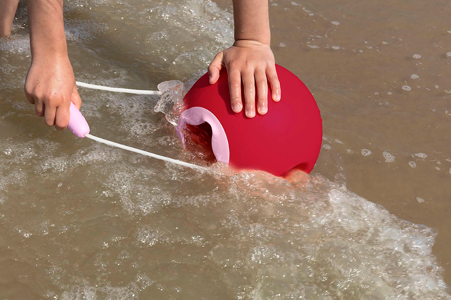 Child scooping up sea water with red bucket