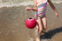 Child in a striped swimsuit holding a pink bucket on a beach