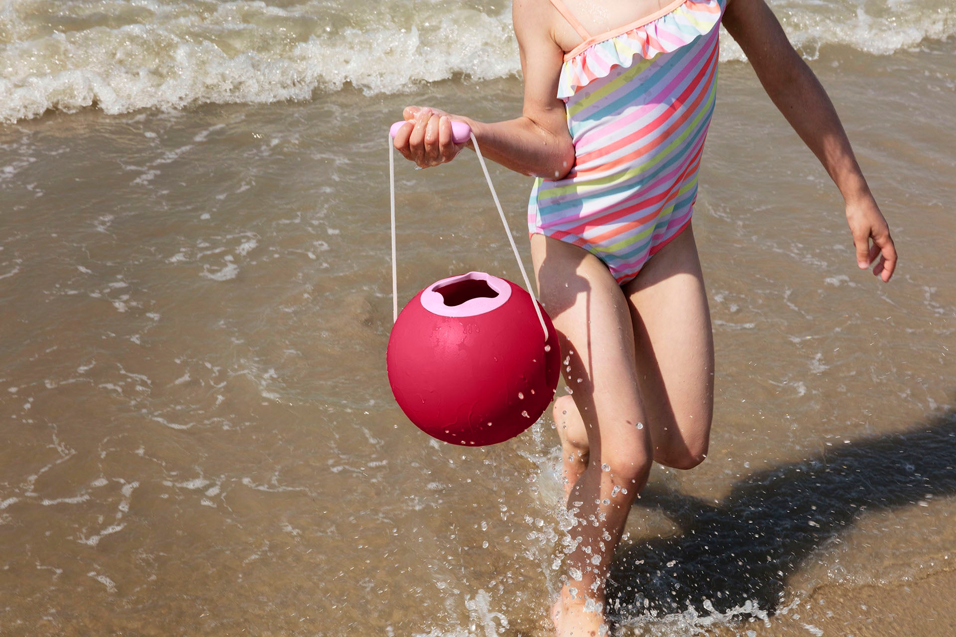 Child in a striped swimsuit holding a pink bucket on a beach