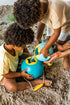 Two children playing with blue and yellow bucket on a sandy beach.