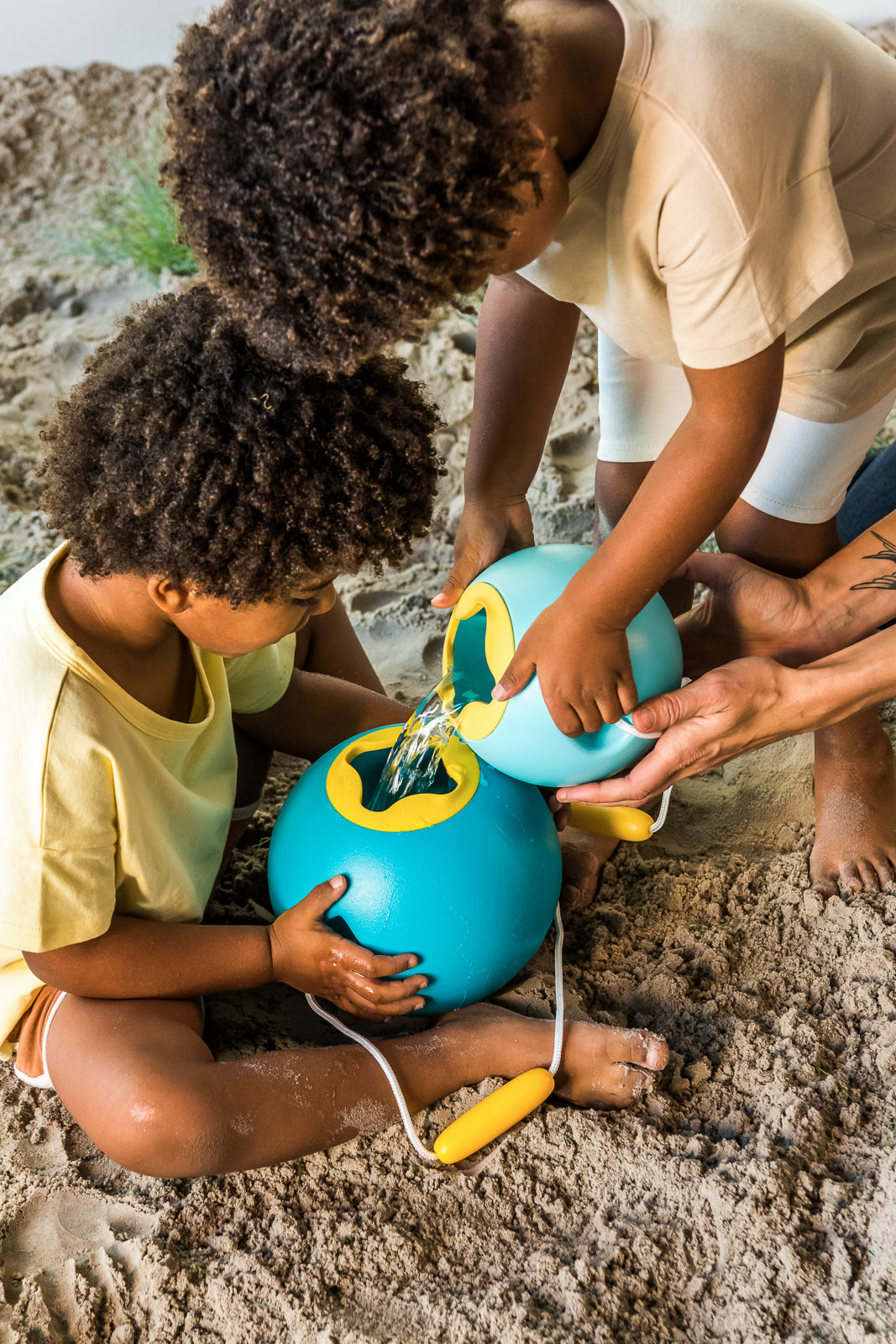 Two children playing with blue and yellow bucket on a sandy beach.