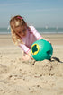 Child playing with a green bucket on a sandy beach