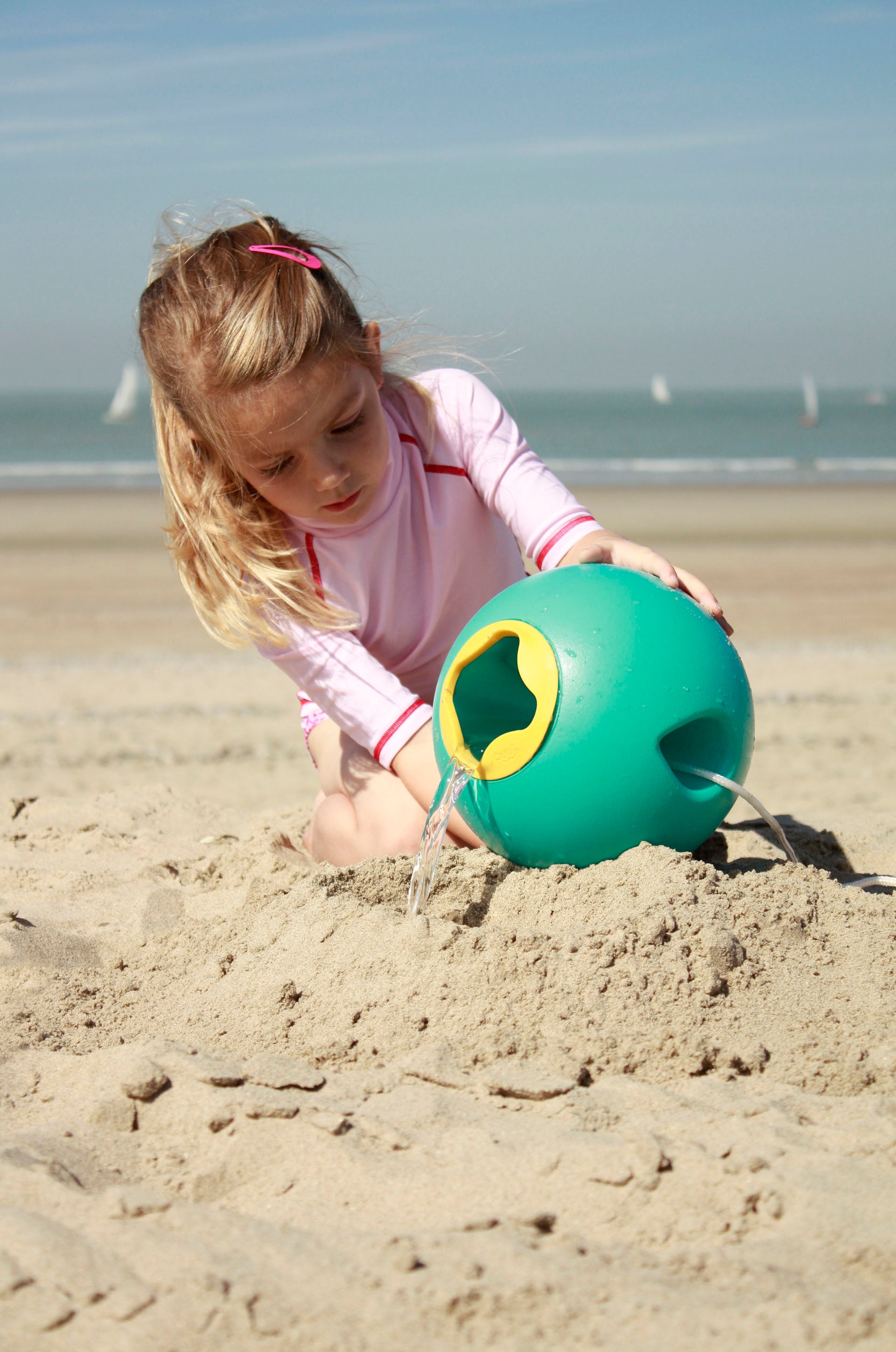 Child playing with a green bucket on a sandy beach