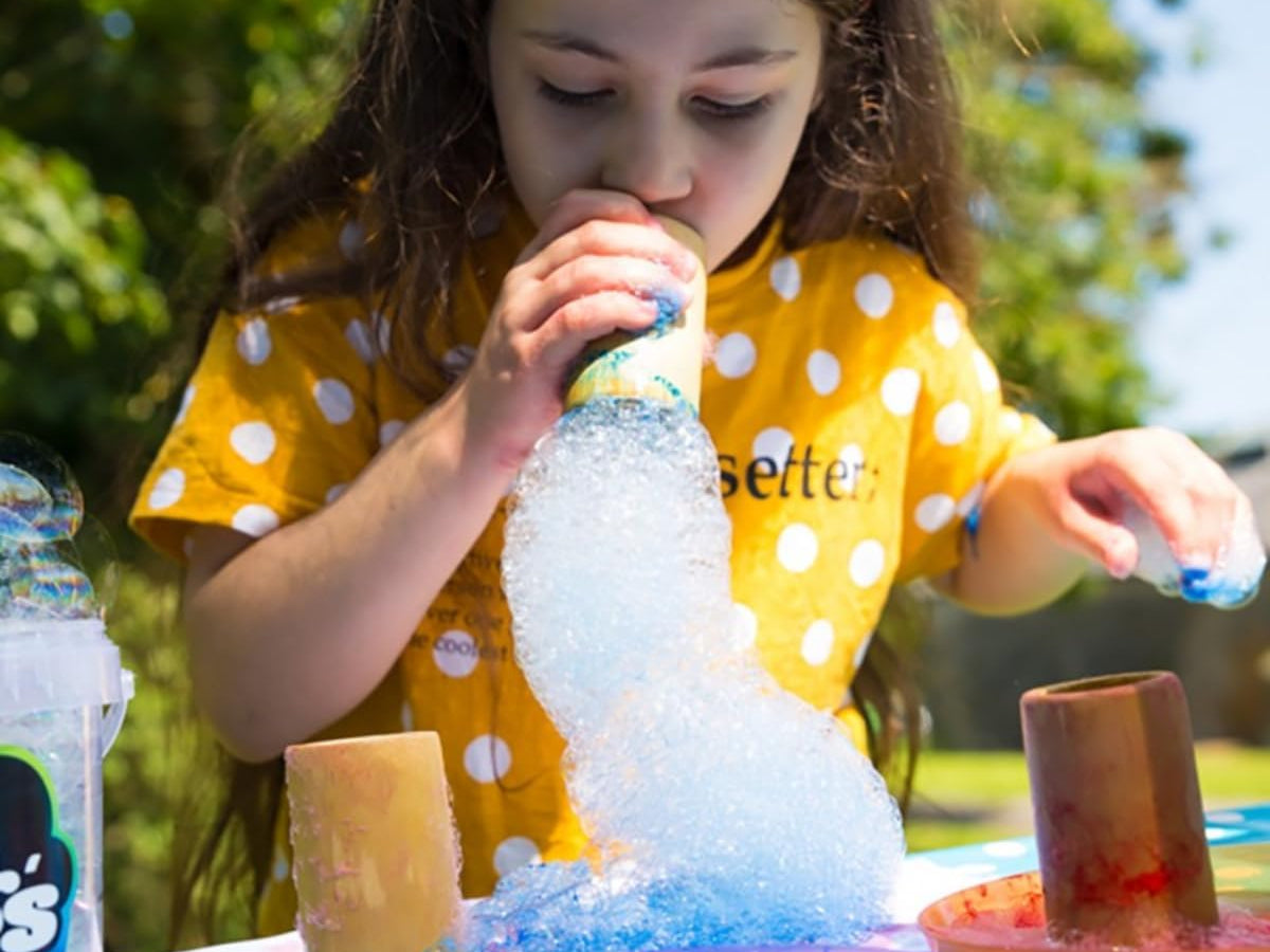 Child playing with bubble solution outdoors, creating a large tube of bubble foam