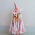 A young girl viewed from behind wearing a pink witch hat with a matching pink cape. The fabric is light pink with tiny white polka dots and subtle glitter, and the hat is adorned with a large pink bow.