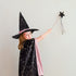 A young girl wearing a black witch hat with gold stars and a matching black cape with gold moon patterns, draped in a pink fabric, holding a black star wand against a plain light gray background.