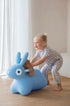 Child playing with a ride on blue inflatable bunny toy indoors.