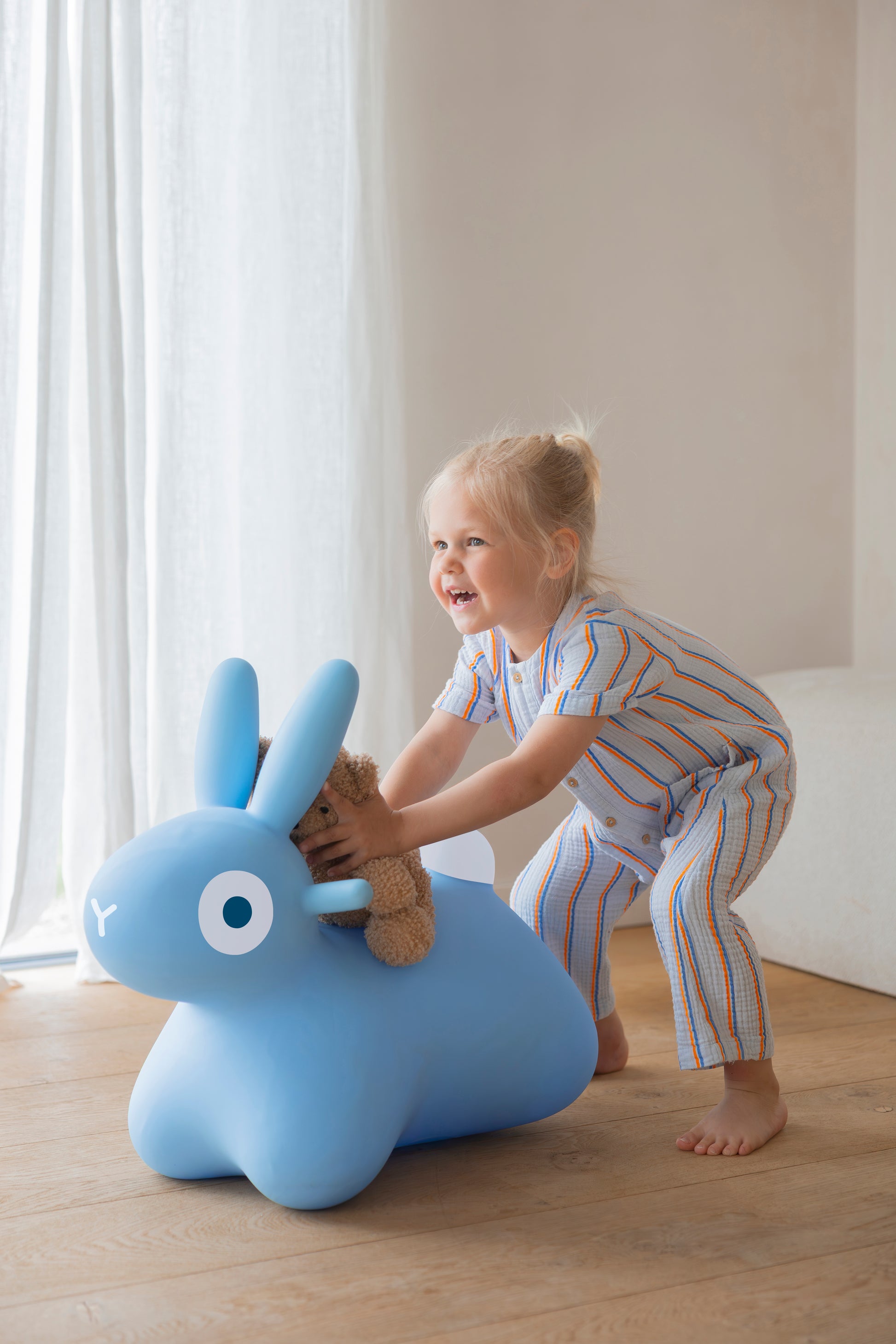 Child playing with a ride on blue inflatable bunny toy indoors.
