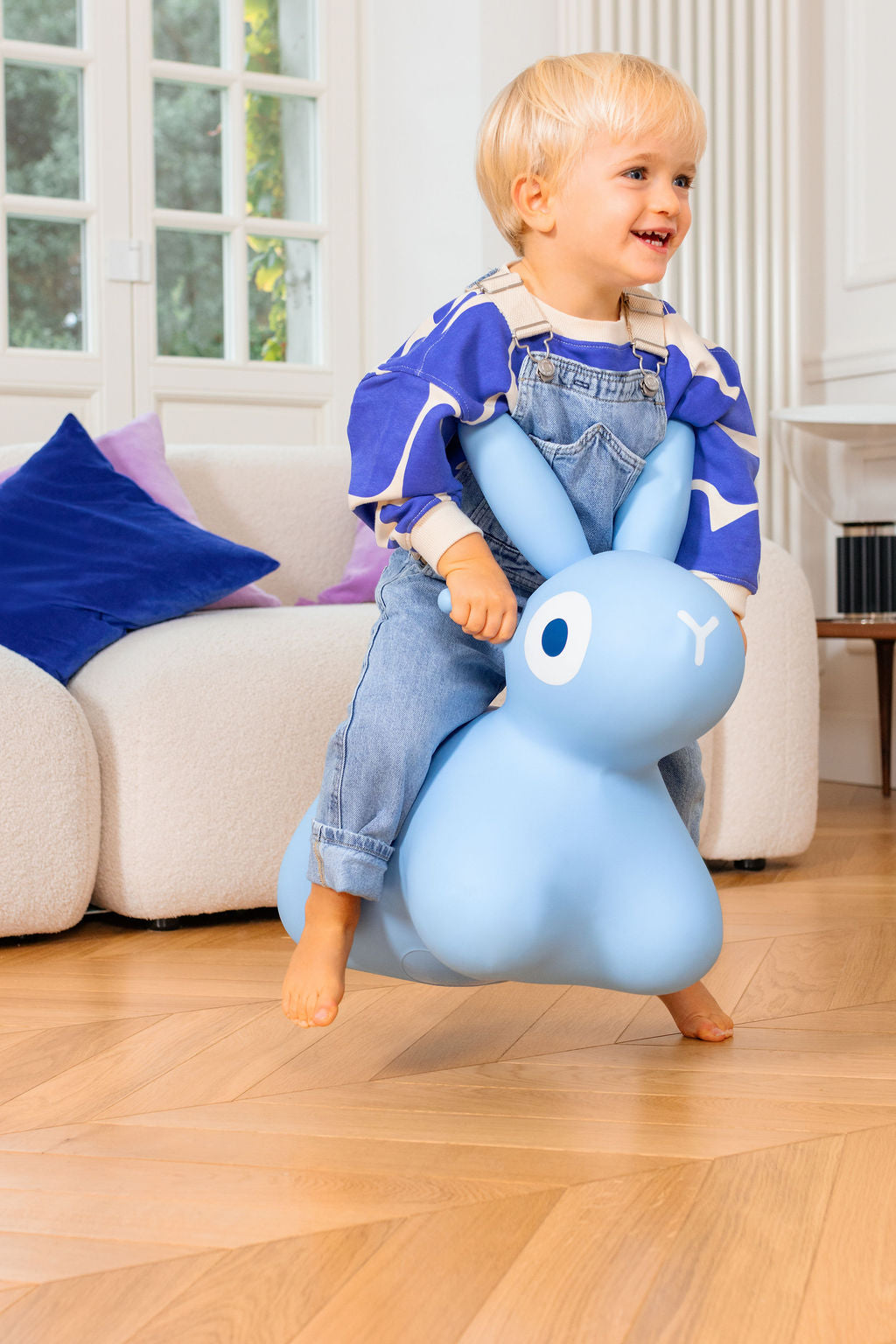 Child riding a blue inflatable bunny toy in a living room.