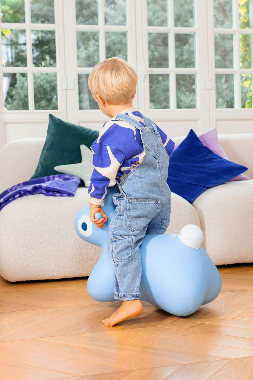 Child sitting on a blue bunny-shaped inflatable toy in a living room.
