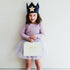 Child wearing a purple outfit with a blue velvet, star-patterned crown, holding a light green box.