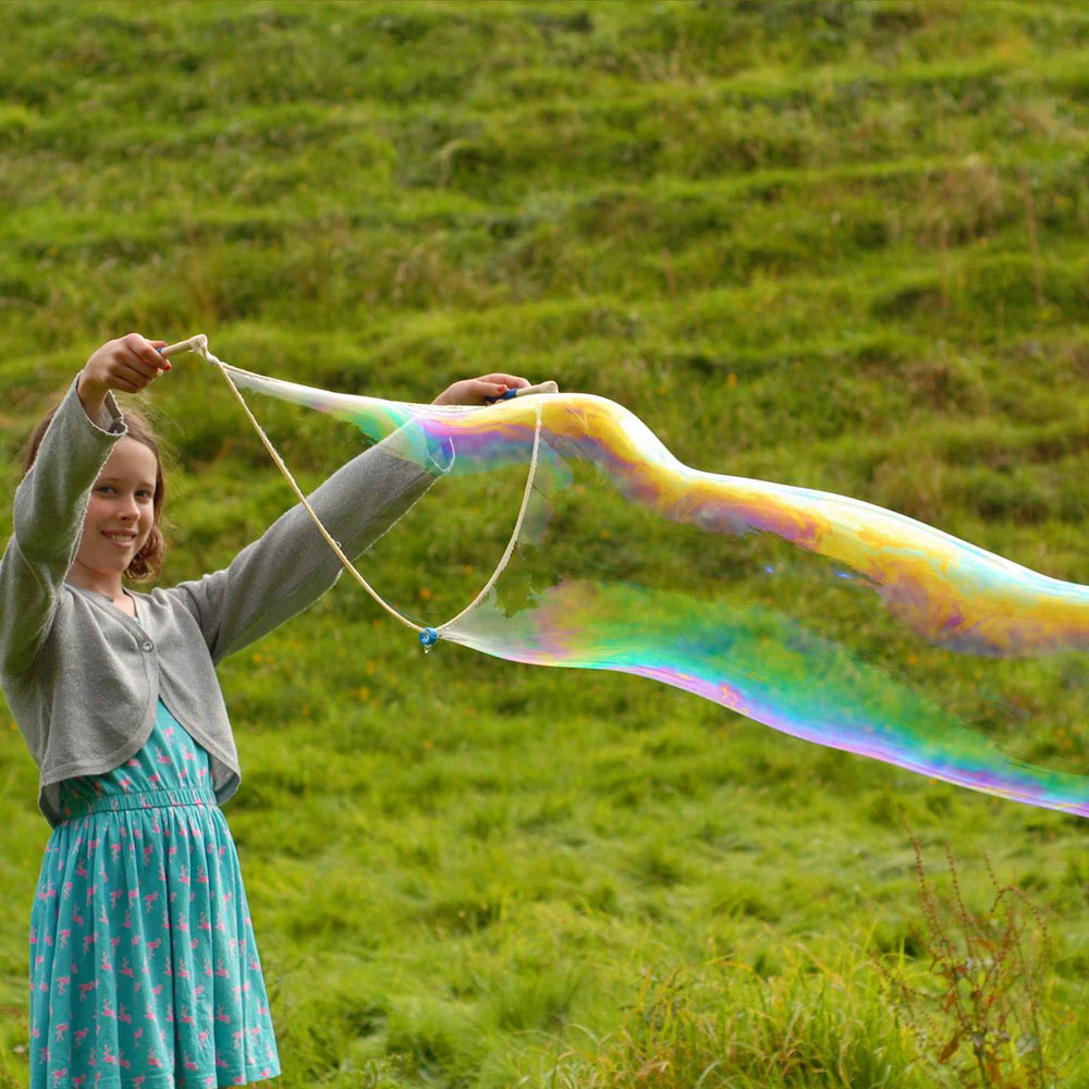 Person blowing large soap bubbles in a grassy field