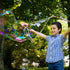 Child blowing large soap bubbles outdoors with trees in the background