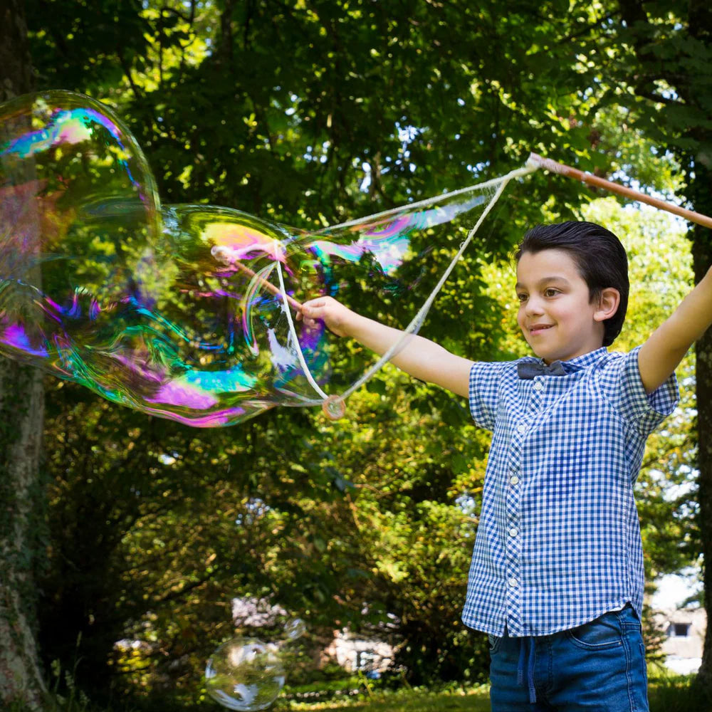 Child blowing large soap bubbles outdoors with trees in the background