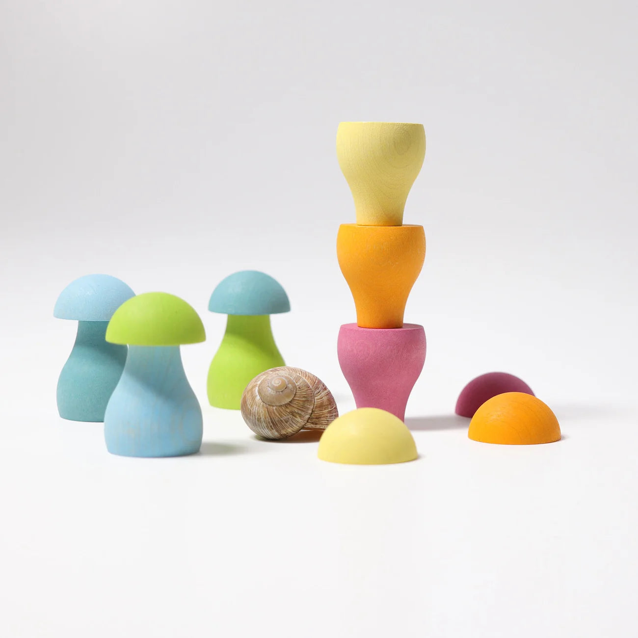 A set of pastel wooden toy mushrooms and matching caps arranged on a clean white studio background. The toys include light blue, lime green, mint green, pink, yellow, orange, and purple pieces, with one natural snail shell included.