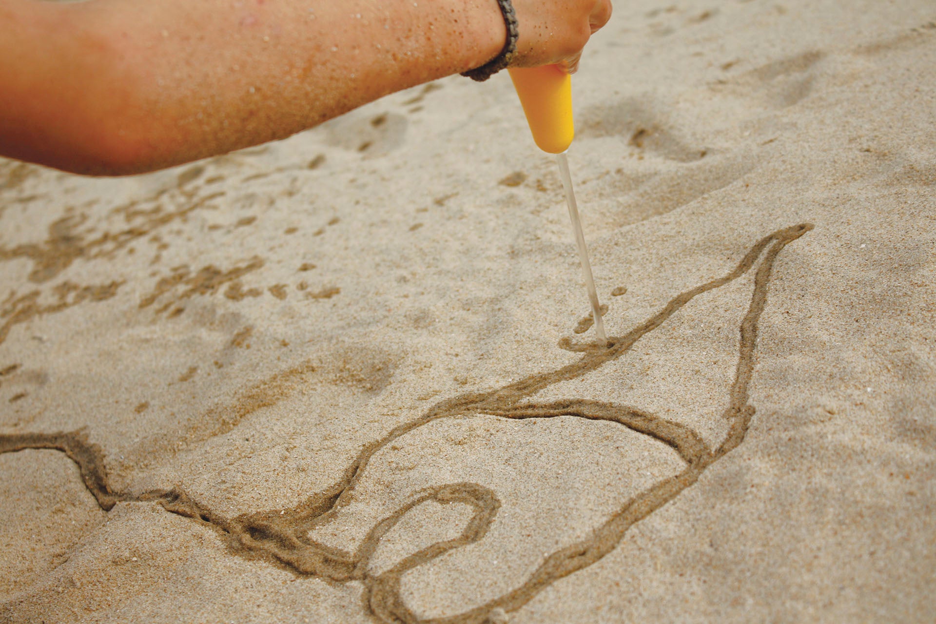 Person drawing on sand with a yellow tool