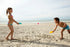 Two children playing with cup and ball on a sandy beach.