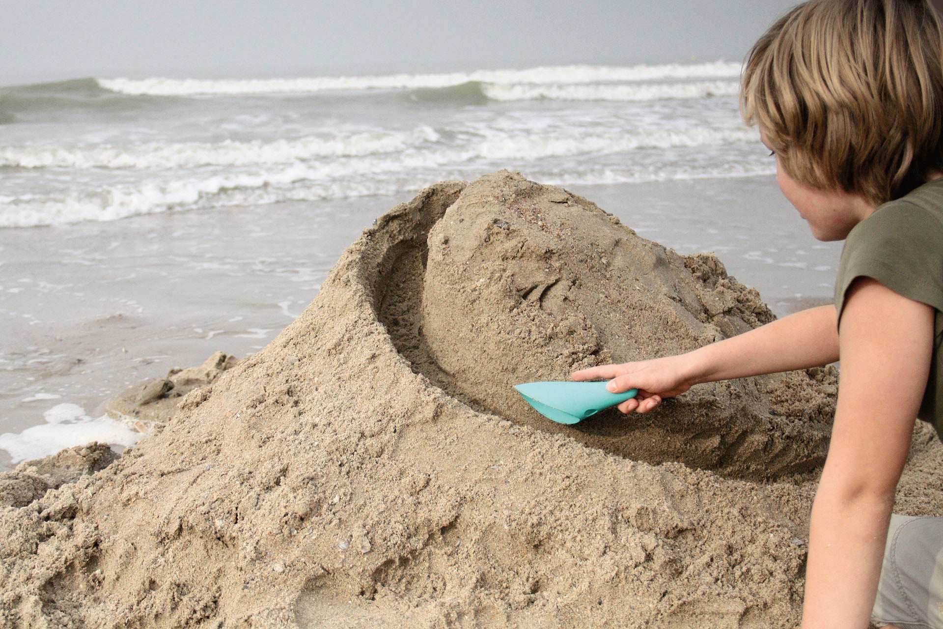 Child building a sandcastle on a beach with ocean waves in the background