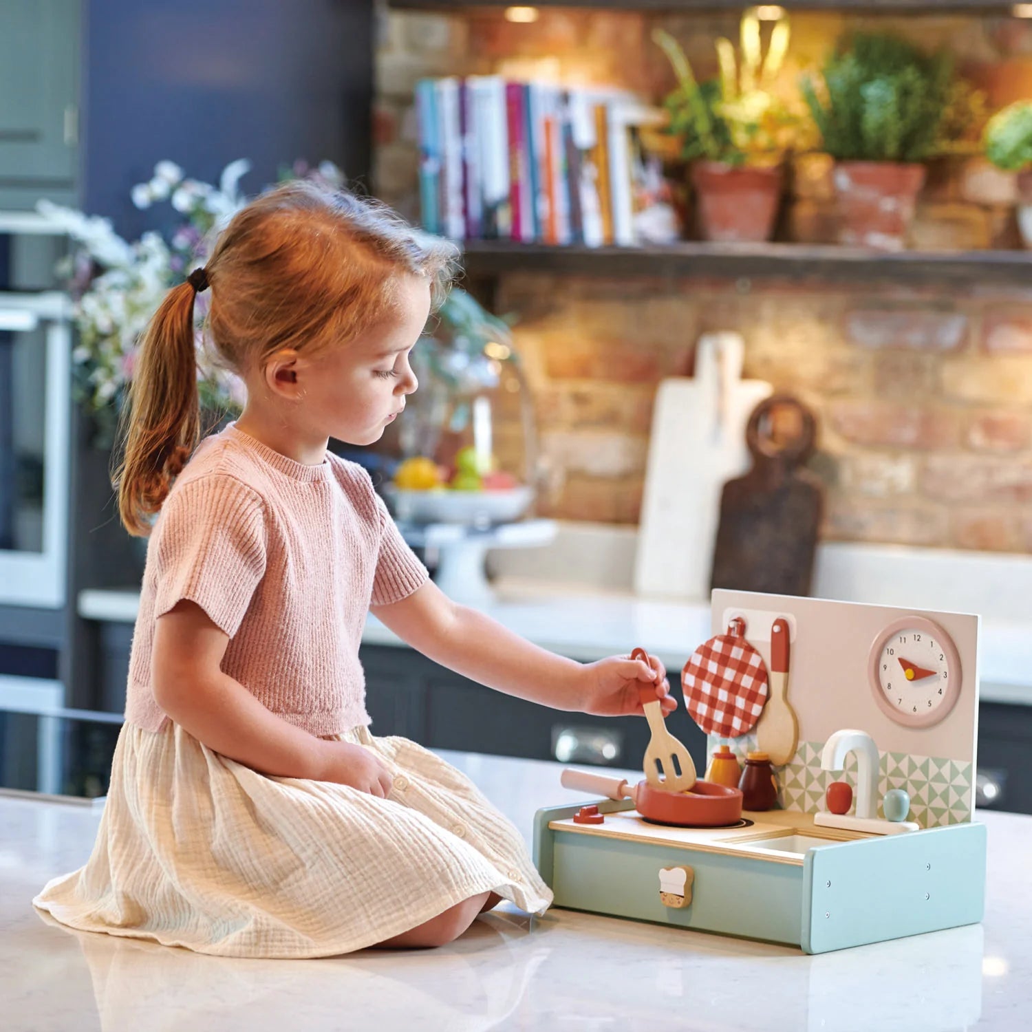 Child playing with a small portable toy kitchen set whilst sat on a kitchen countertop