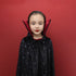 A young girl wearing a black vampire cape with silver star patterns and a red inner collar, posing against a solid red background.