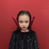 A young girl with slicked-back dark hair wearing a black vampire cape with silver star patterns and a red inner collar, posing against a solid red background.