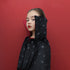 A young girl wearing a black hooded cape with a silver star pattern, posed against a solid red background.